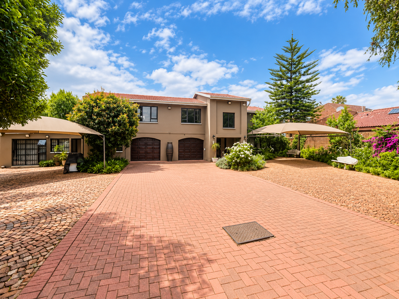 Spacious front exterior featuring a large paved driveway, double garage, and established garden with shade sail structures for vehicle protection.