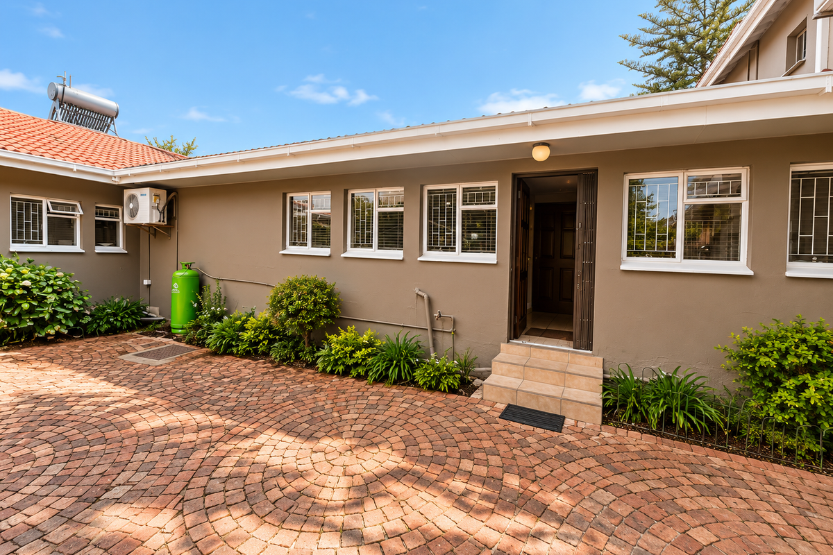 A well-maintained rear courtyard featuring patterned brick paving, secure entrance access, and integrated exterior fixtures including a solar water heater and air conditioning unit.