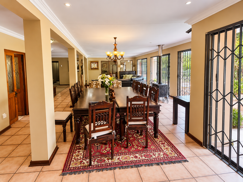 Spacious open-plan dining and living area featuring tiled flooring, a freestanding fireplace, and large sliding doors with security gates leading to the exterior.