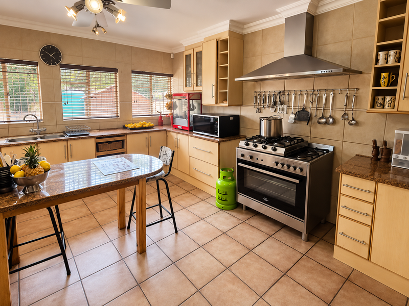 A well-maintained kitchen featuring light wood cabinetry, granite countertops, a stainless steel gas stove with extractor fan, and tiled flooring throughout.