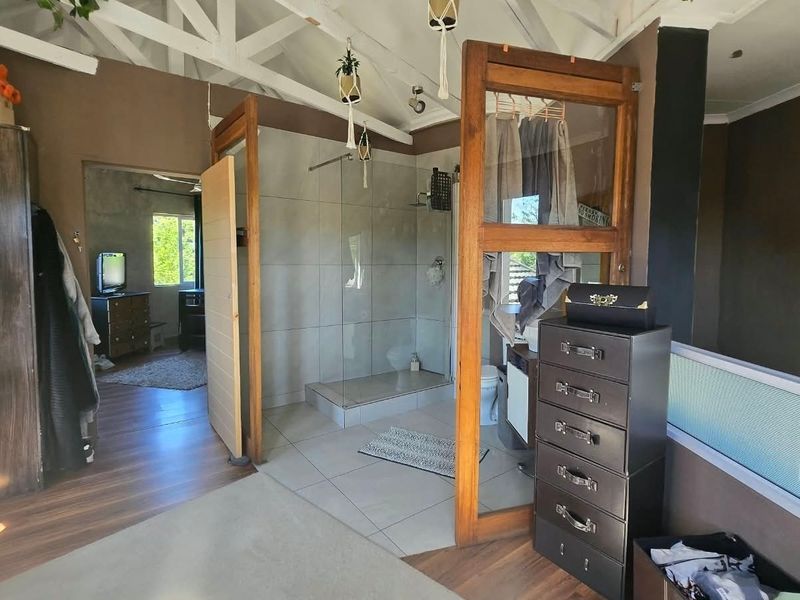 An open-plan bathroom area featuring a walk-in shower with glass screen, tiled flooring, and exposed white-painted roof trusses.