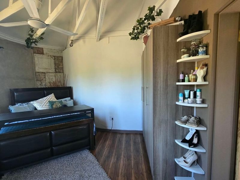 A bedroom featuring a vaulted ceiling with exposed rafters, a ceiling fan, laminate flooring, and a built-in wardrobe with integrated shelving.