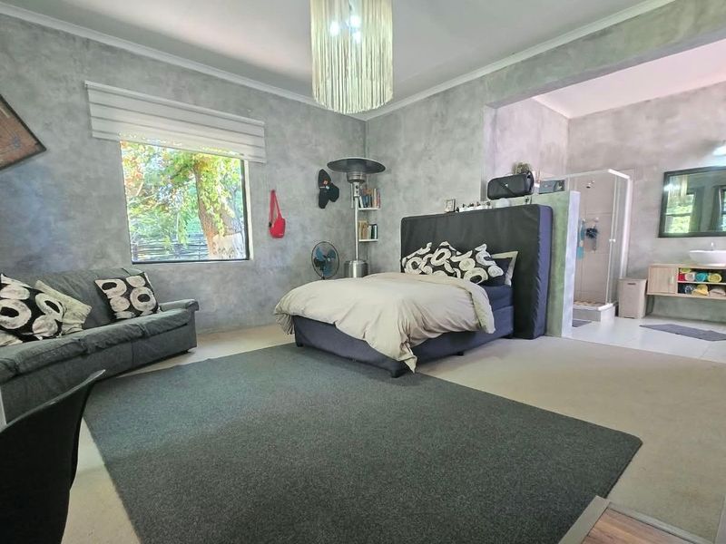 Spacious bedroom featuring an open-plan en-suite bathroom with a shower and vanity, complemented by modern wall finishes and large windows.