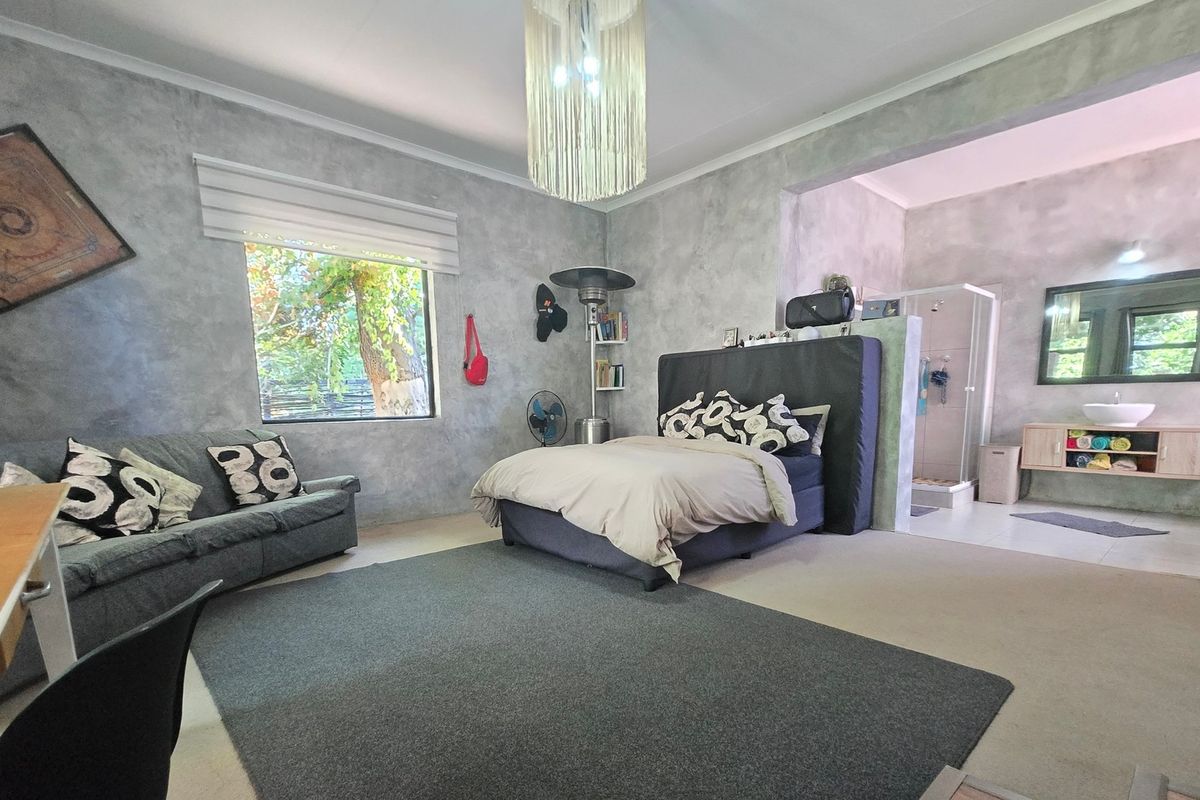 Spacious bedroom featuring a modern cement-finish aesthetic, an open-plan en-suite shower area, and a built-in vanity unit.