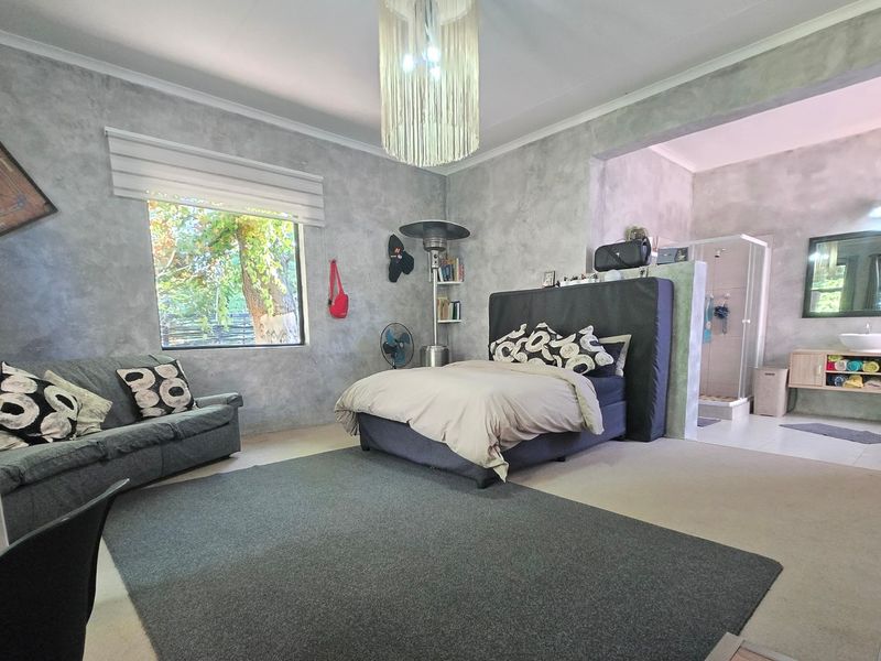 Spacious bedroom featuring a modern cement-finish aesthetic, an open-plan en-suite shower area, and a built-in vanity unit.