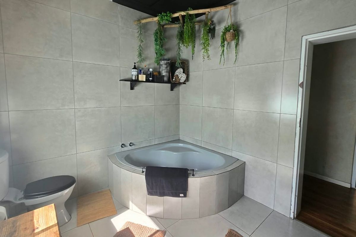 A modern bathroom featuring large format wall tiles, a corner bathtub, and a standard toilet.