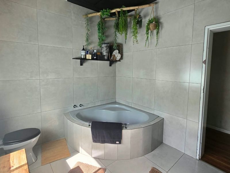 A modern bathroom featuring large format wall tiles, a corner bathtub, and a standard toilet.