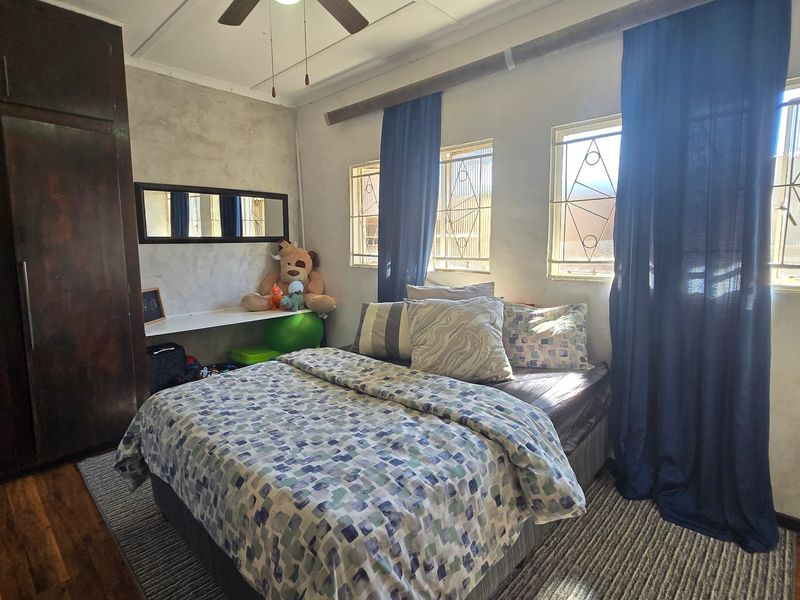 A bedroom featuring a built-in wardrobe, ceiling fan, and windows fitted with security bars.