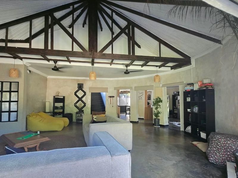 Spacious open-plan living area featuring high vaulted ceilings with exposed timber trusses, concrete flooring, and a central wood-burning fireplace.