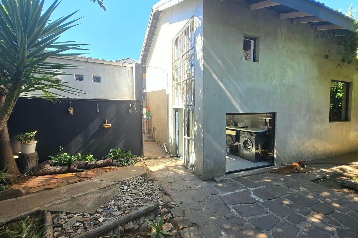 Rear exterior view of the property featuring stone paving, a concrete facade, and an integrated laundry area accessible from the garden.