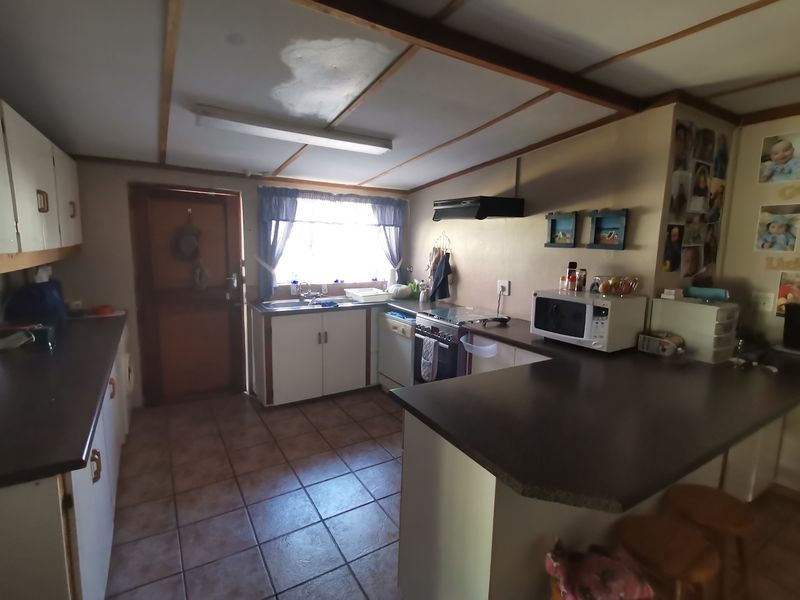 A functional kitchen featuring built-in cabinetry, laminate countertops, a freestanding stove with extractor fan, and tiled flooring, showing signs of wear and ceiling water damage.