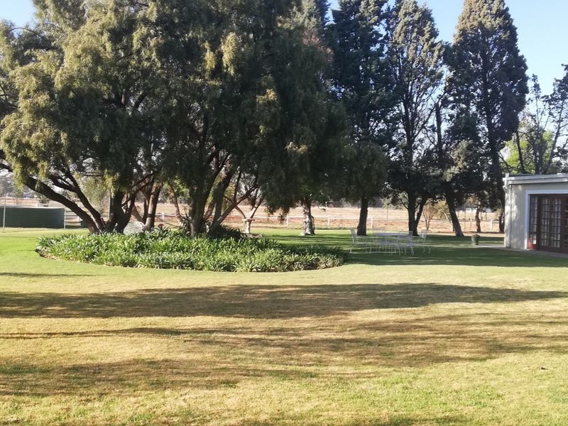 A spacious, well-maintained garden area featuring mature trees, manicured lawn, and established garden beds adjacent to the property structure.