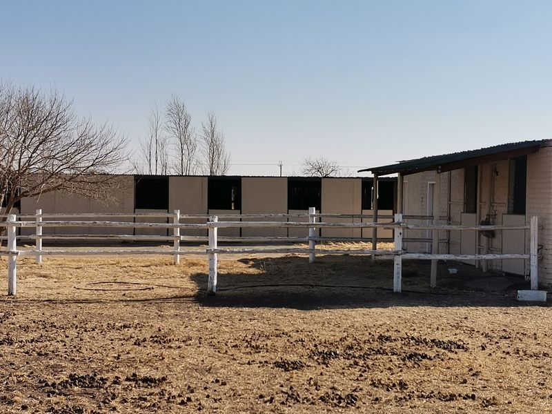 Exterior view of industrial-style horse stables featuring masonry construction, corrugated metal roofing, and perimeter post and rail fencing.