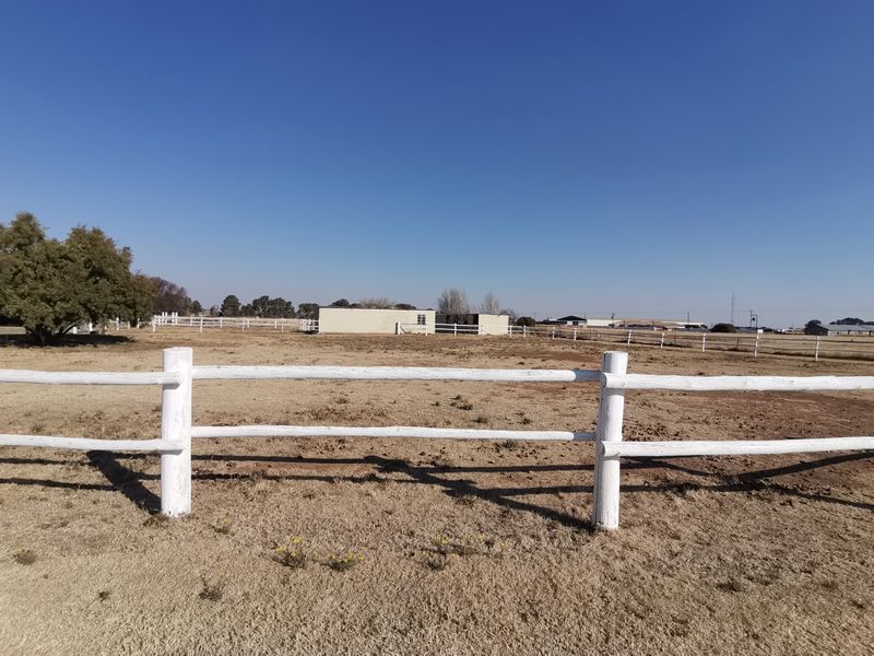 Expansive industrial property grounds featuring post and rail perimeter fencing and a detached outbuilding under a clear blue sky.