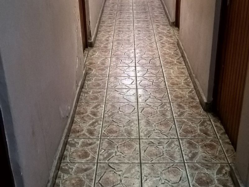 A long commercial hallway featuring patterned ceramic tile flooring and multiple wooden doors leading to individual rooms.