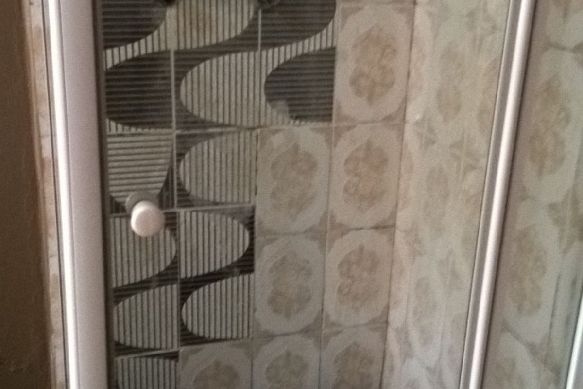A compact shower stall featuring a glass enclosure, overhead shower fixture, and mixed decorative wall tiling.