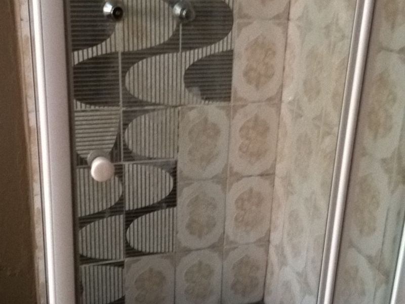 A compact shower stall featuring a glass enclosure, overhead shower fixture, and mixed decorative wall tiling.