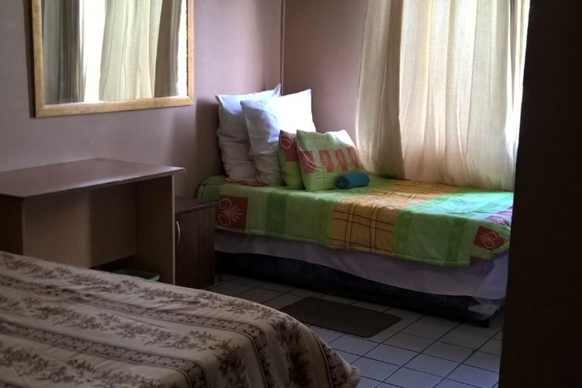 A compact bedroom featuring tiled flooring, a wall-mounted air conditioning unit, and a wall-mounted television bracket, offering a functional layout for accommodation.