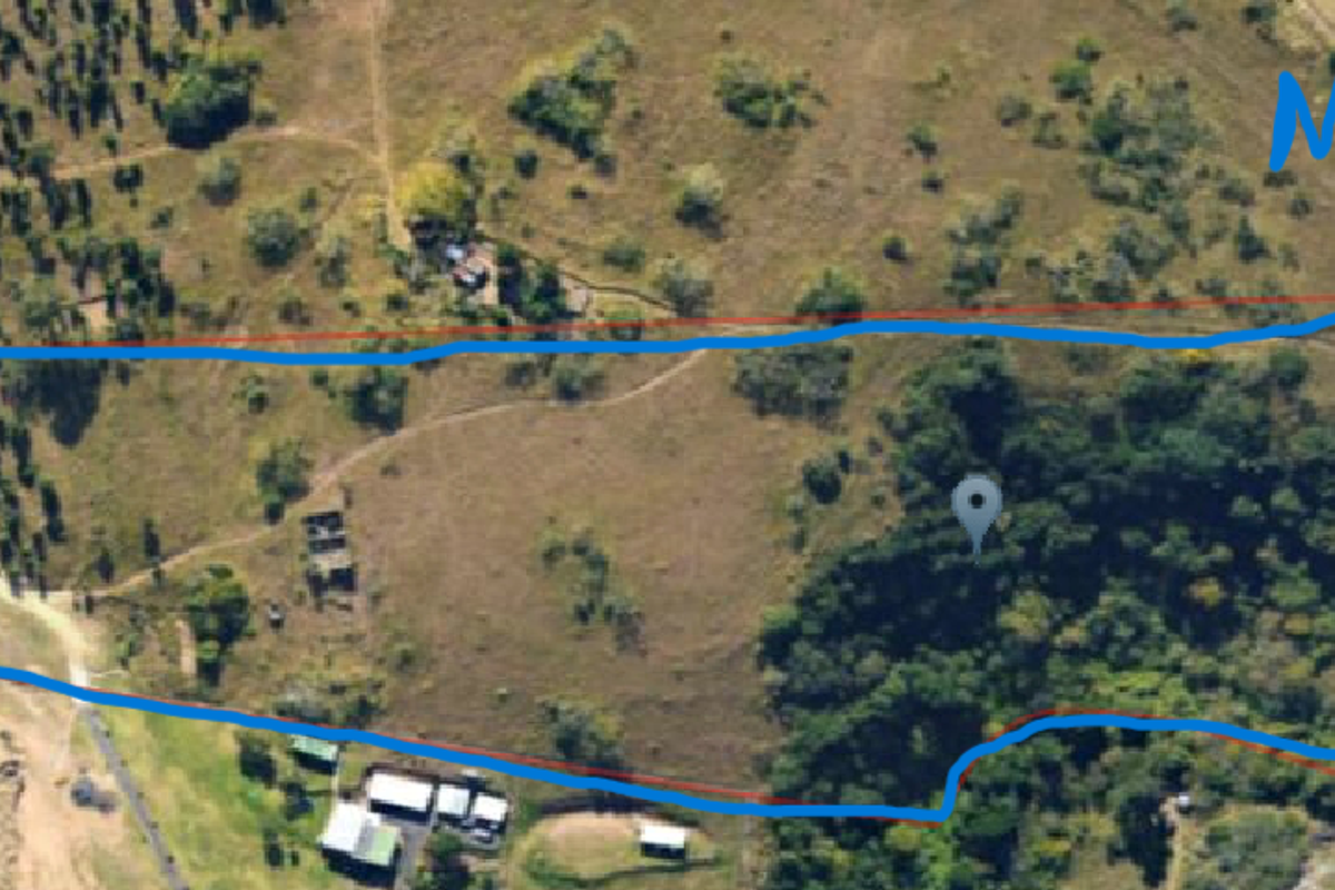 Aerial view of a large, undeveloped residential land parcel featuring natural vegetation and access tracks, located near a major highway.