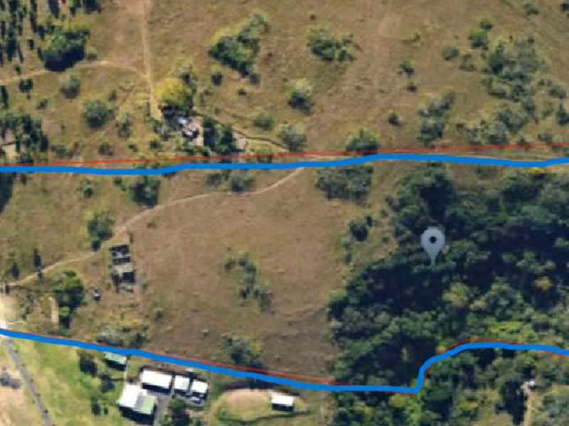 Aerial view of a large, undeveloped residential land parcel featuring natural vegetation and access tracks, located near a major highway.