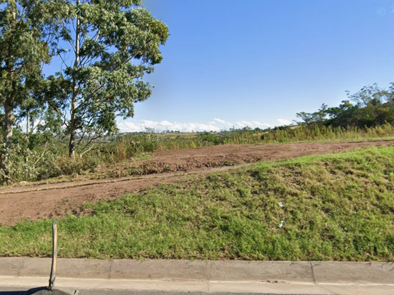 A vacant residential plot featuring a sloped landscape and concrete curb, offering potential for future development.
