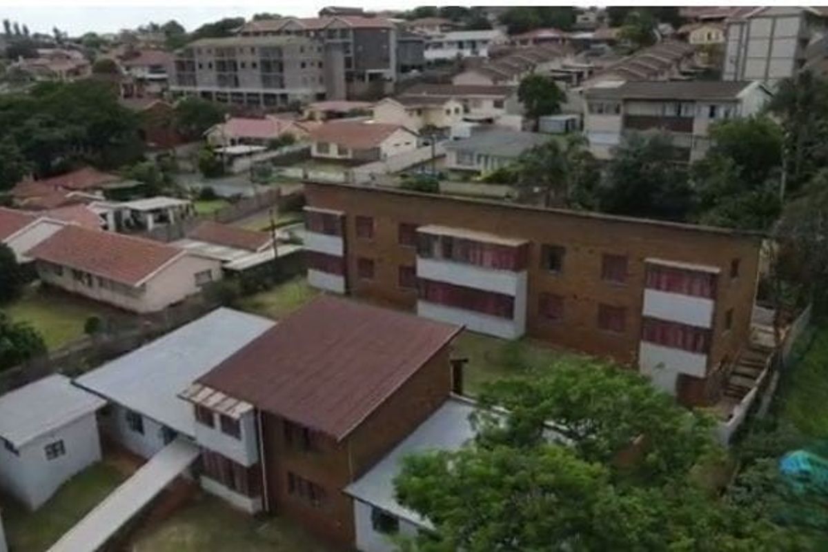 An aerial view of the apartment complex and surrounding residential neighborhood, showcasing the building's exterior structure and site layout.
