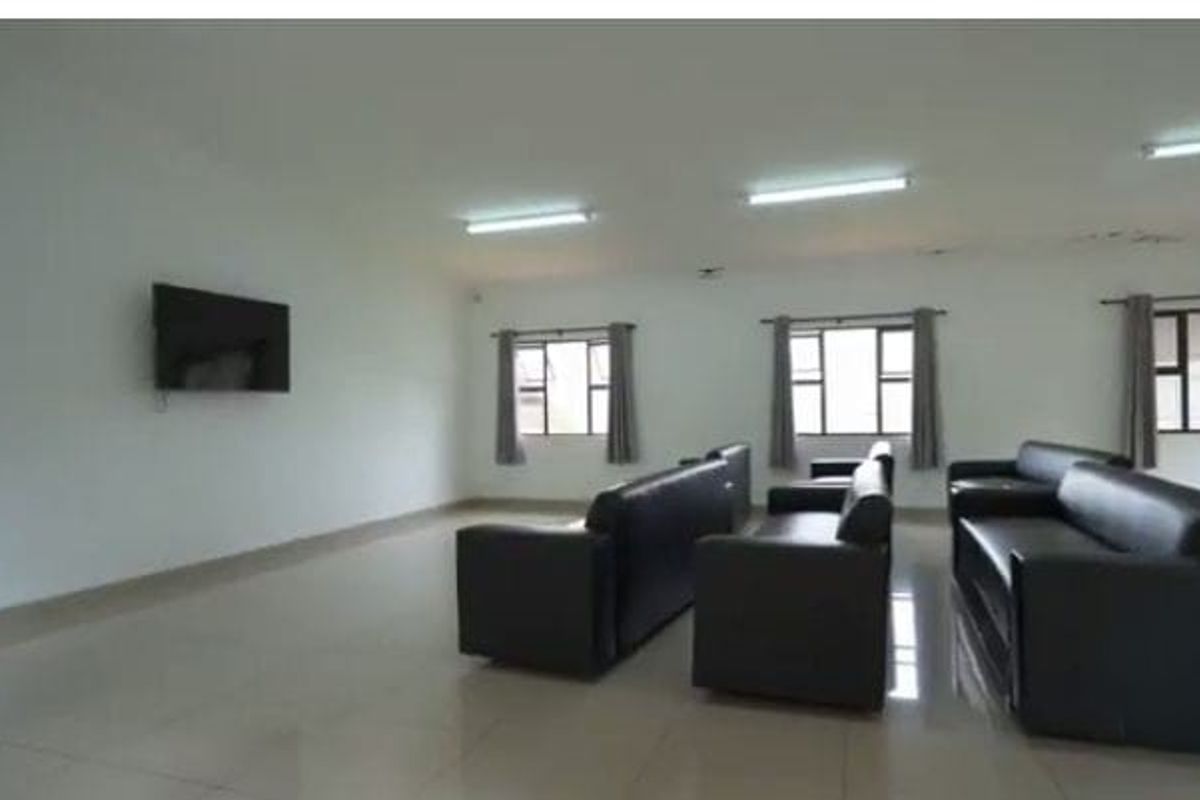 Spacious living area featuring tiled flooring, multiple windows, and fluorescent lighting, showing signs of ceiling water damage.