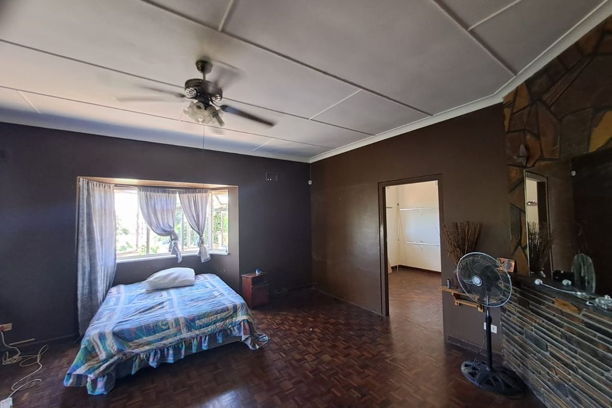 Spacious bedroom featuring original parquet flooring, a stone-clad fireplace, and a ceiling fan, offering a classic layout with an adjoining walk-in closet area.