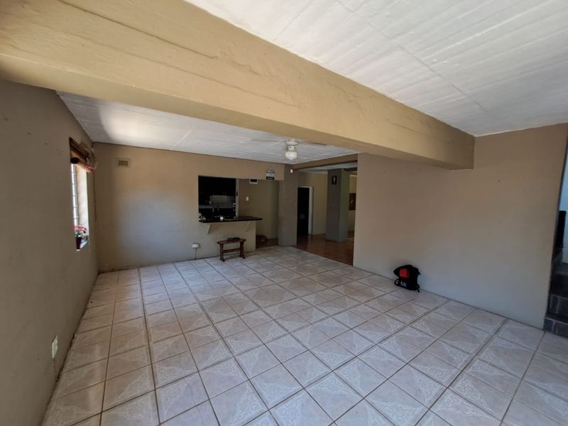 An empty, open-plan living area featuring tiled flooring, a ceiling fan, and a convenient pass-through window connecting to the kitchen space.