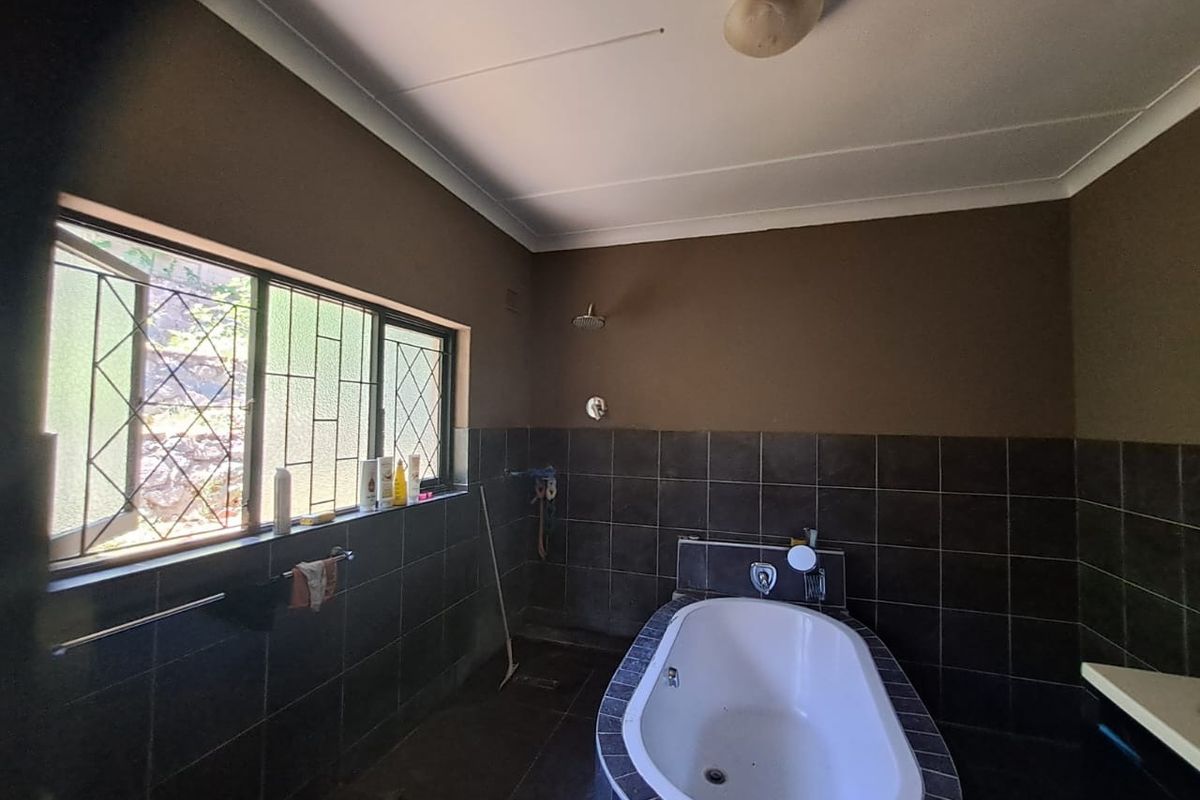 A functional bathroom featuring a built-in bathtub, wall-mounted shower head, and dark tiled wall finishes with security-barred windows.
