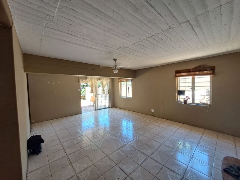 Spacious, empty living area featuring tiled flooring, a ceiling fan, and natural light through windows with security bars and access to an outdoor area.