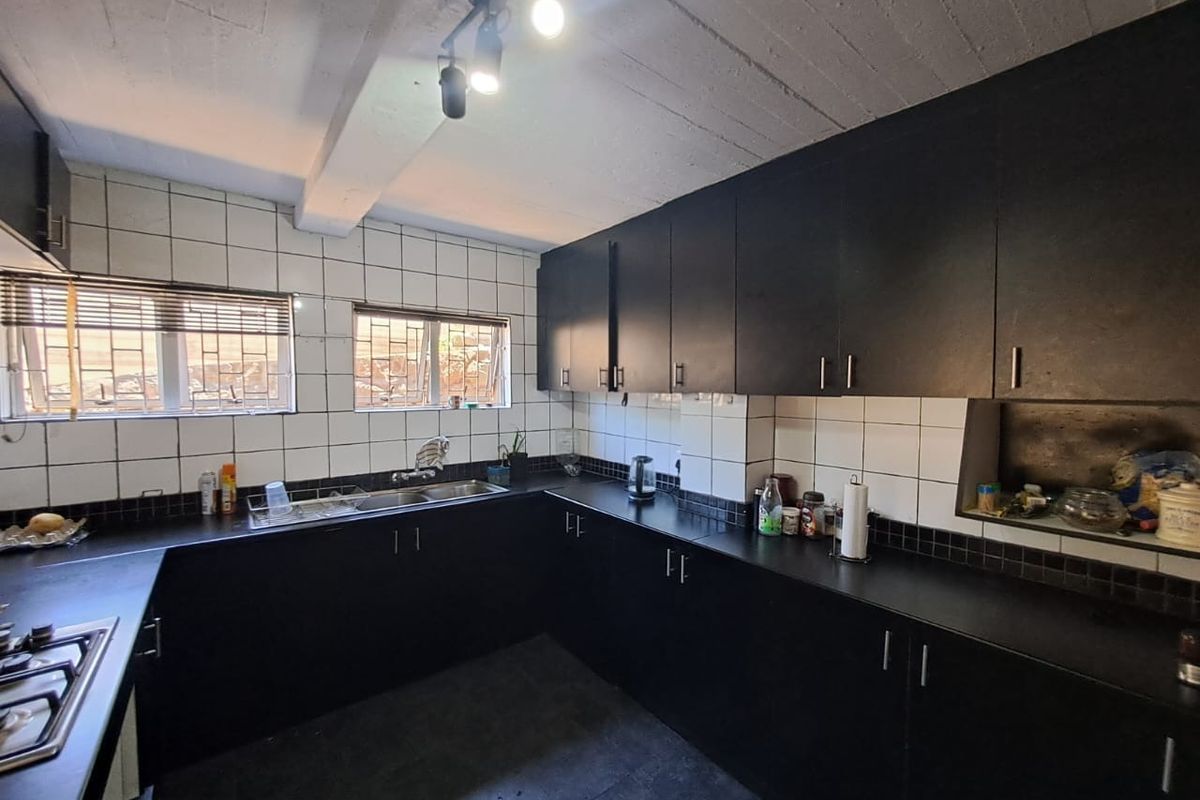 A functional kitchen featuring dark cabinetry, contrasting white tiled backsplash, integrated hob, and exposed beam ceiling, offering a solid foundation for modern updates.