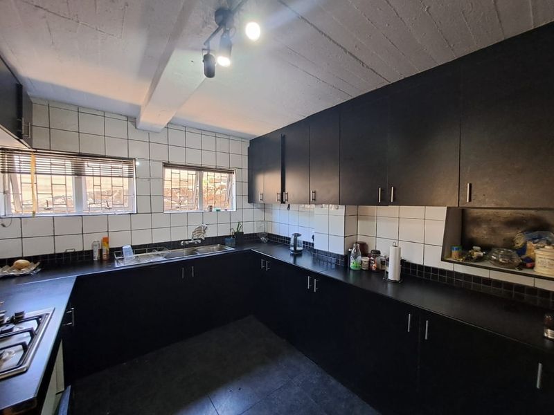 A functional kitchen featuring dark cabinetry, contrasting white tiled backsplash, integrated hob, and exposed beam ceiling, offering a solid foundation for modern updates.