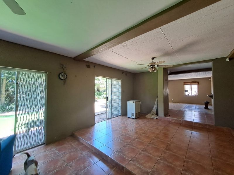 Spacious open-plan living area featuring ceramic tile flooring, a raised floor section, and sliding security doors leading to the garden.
