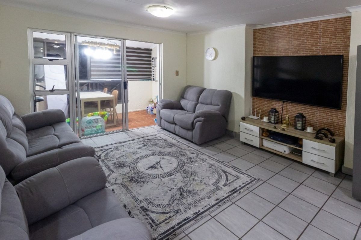 A spacious living room featuring tiled flooring, a brick-style feature wall, and a sliding glass door providing access to an outdoor balcony area.