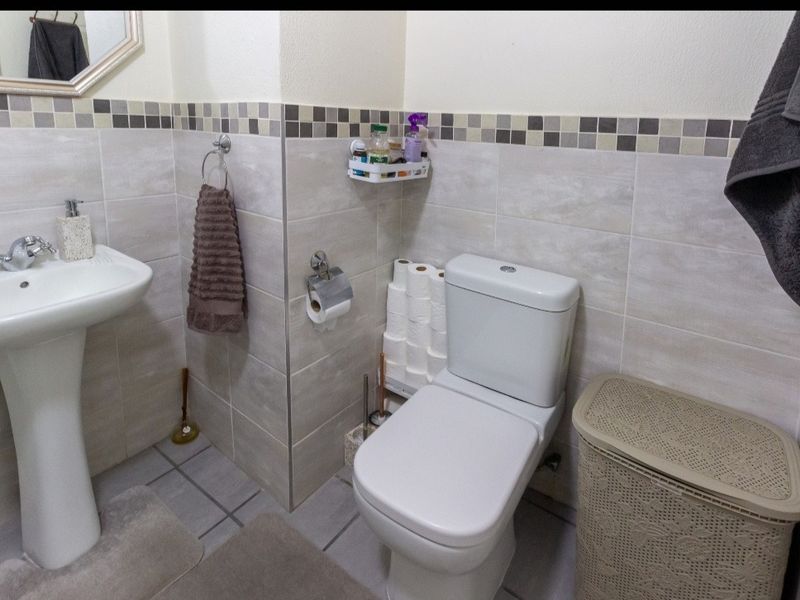 A functional bathroom featuring a pedestal sink, a standard toilet, and neutral wall tiling with a decorative mosaic border.