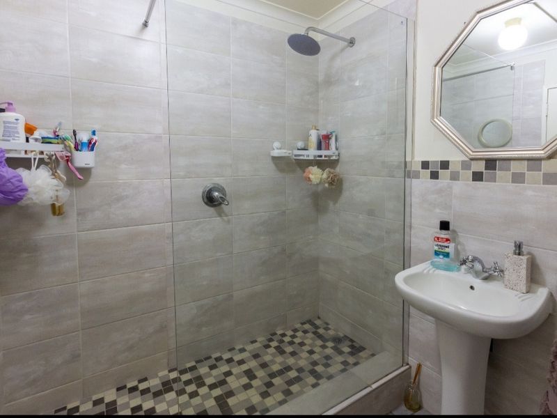 A modern bathroom featuring a walk-in shower with a rainfall shower head, glass screen, and a pedestal sink with a decorative wall mirror.
