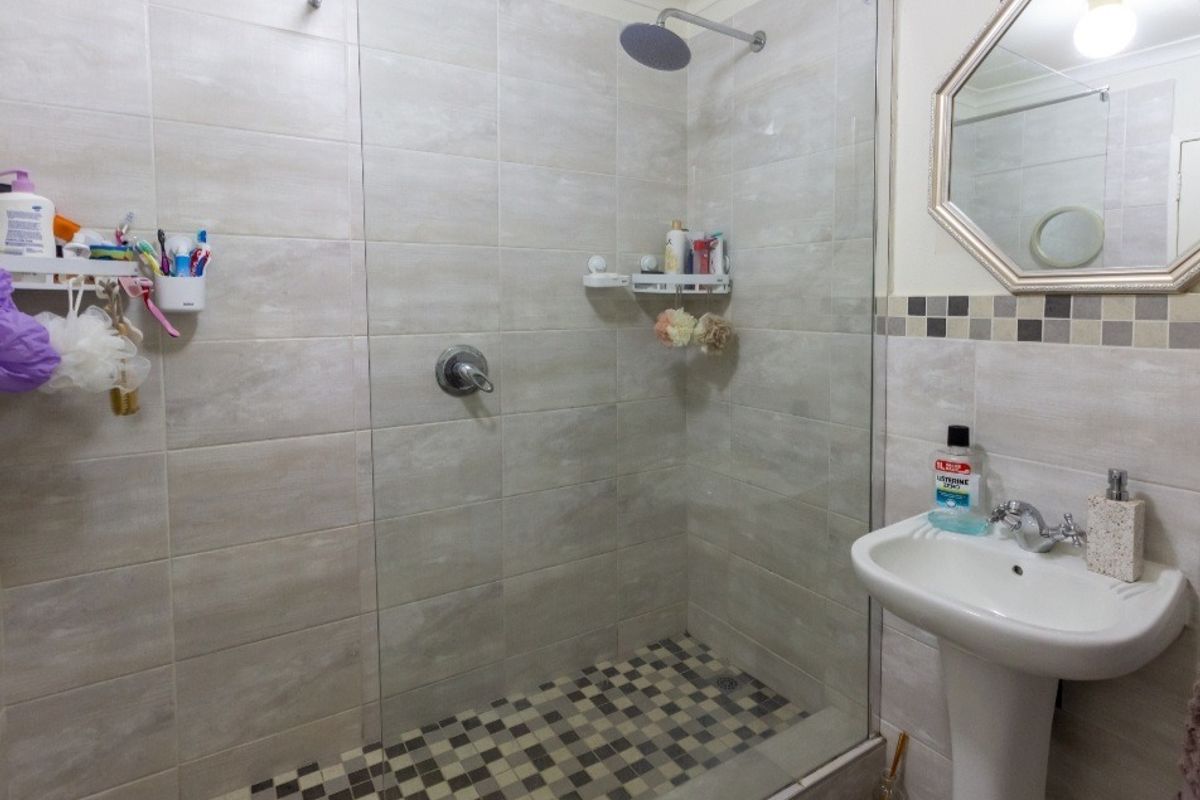 A modern bathroom featuring a walk-in shower with a rainfall shower head, glass screen, and a pedestal sink with a decorative wall mirror.