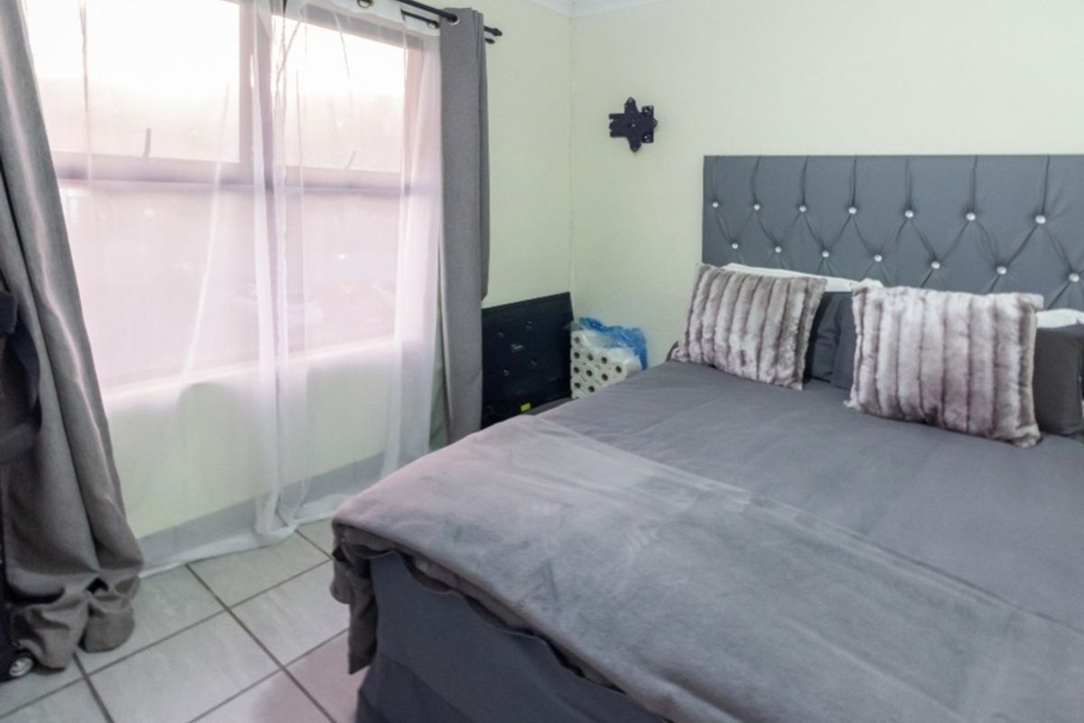 A bedroom featuring tiled flooring and a wall-mounted television bracket, providing a functional space with natural light from the window.