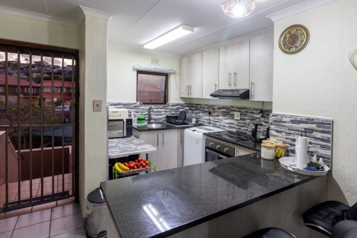 Compact kitchen featuring granite countertops, built-in cabinetry, integrated oven with extractor fan, and a tiled backsplash, with direct access to an outdoor area.