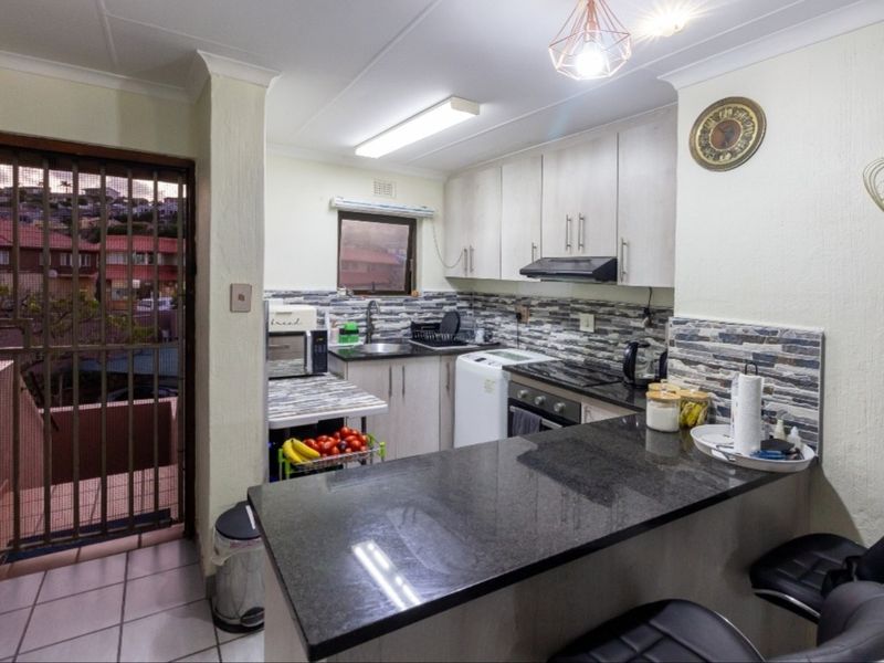 Compact kitchen featuring granite countertops, built-in cabinetry, integrated oven with extractor fan, and a tiled backsplash, with direct access to an outdoor area.