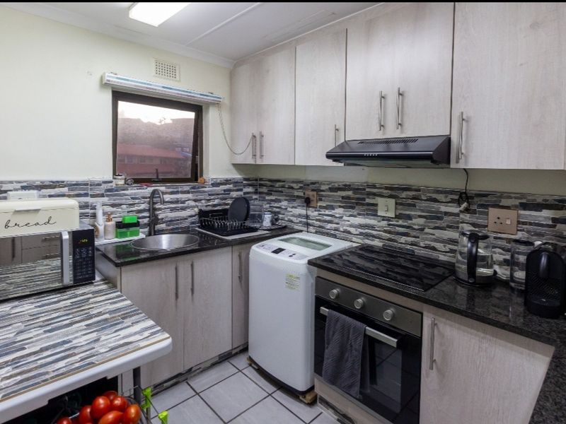 Compact kitchen featuring light wood-finish cabinetry, dark stone countertops, a tiled splashback, and integrated appliances including an oven and extractor fan.