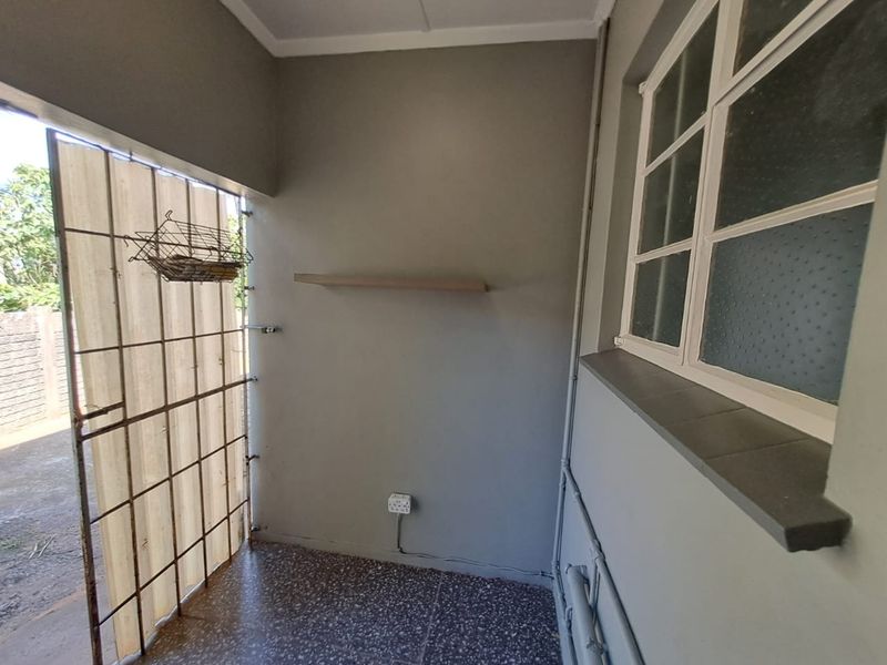 A functional utility or service area featuring tiled flooring, a security gate, and a wall-mounted shelf, suitable for storage or laundry use.