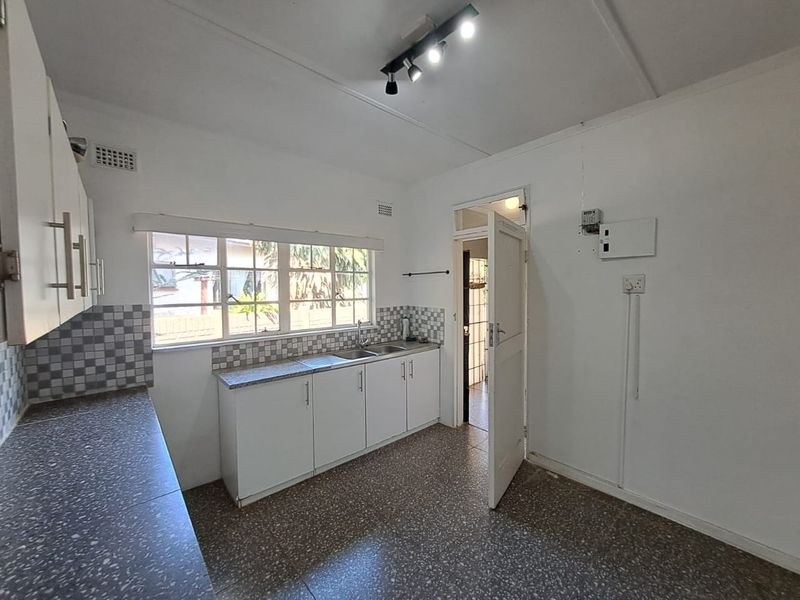 A functional kitchen featuring white cabinetry, laminate countertops, a stainless steel double sink, and terrazzo flooring, offering a clean canvas for potential updates.