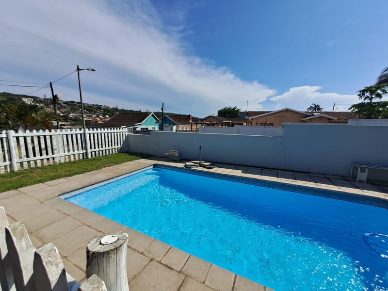 Outdoor swimming pool area featuring paved surround, white picket fencing, and a boundary wall in a residential setting.
