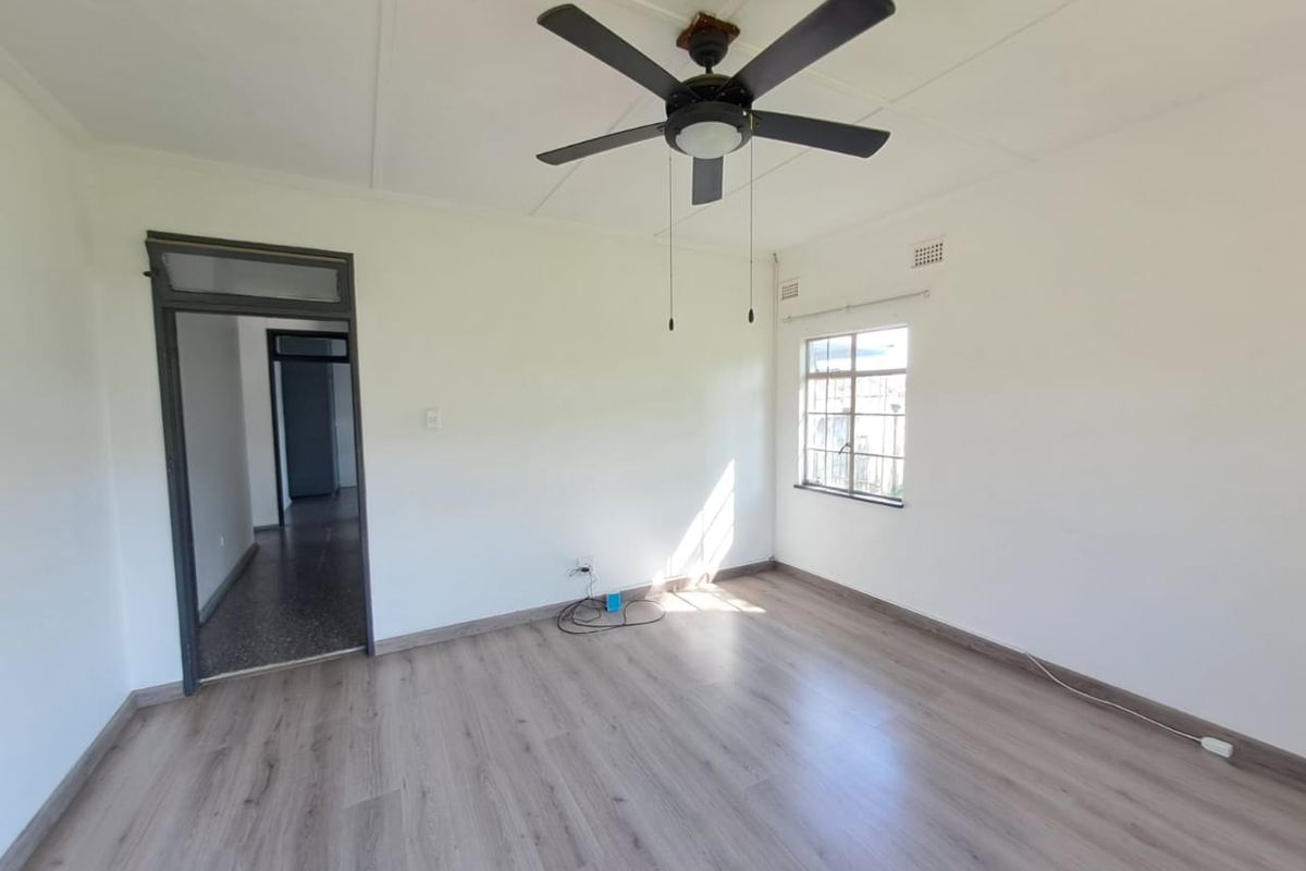 An empty bedroom featuring light-toned laminate flooring, a ceiling fan, and neutral walls, offering a blank canvas for personalization.