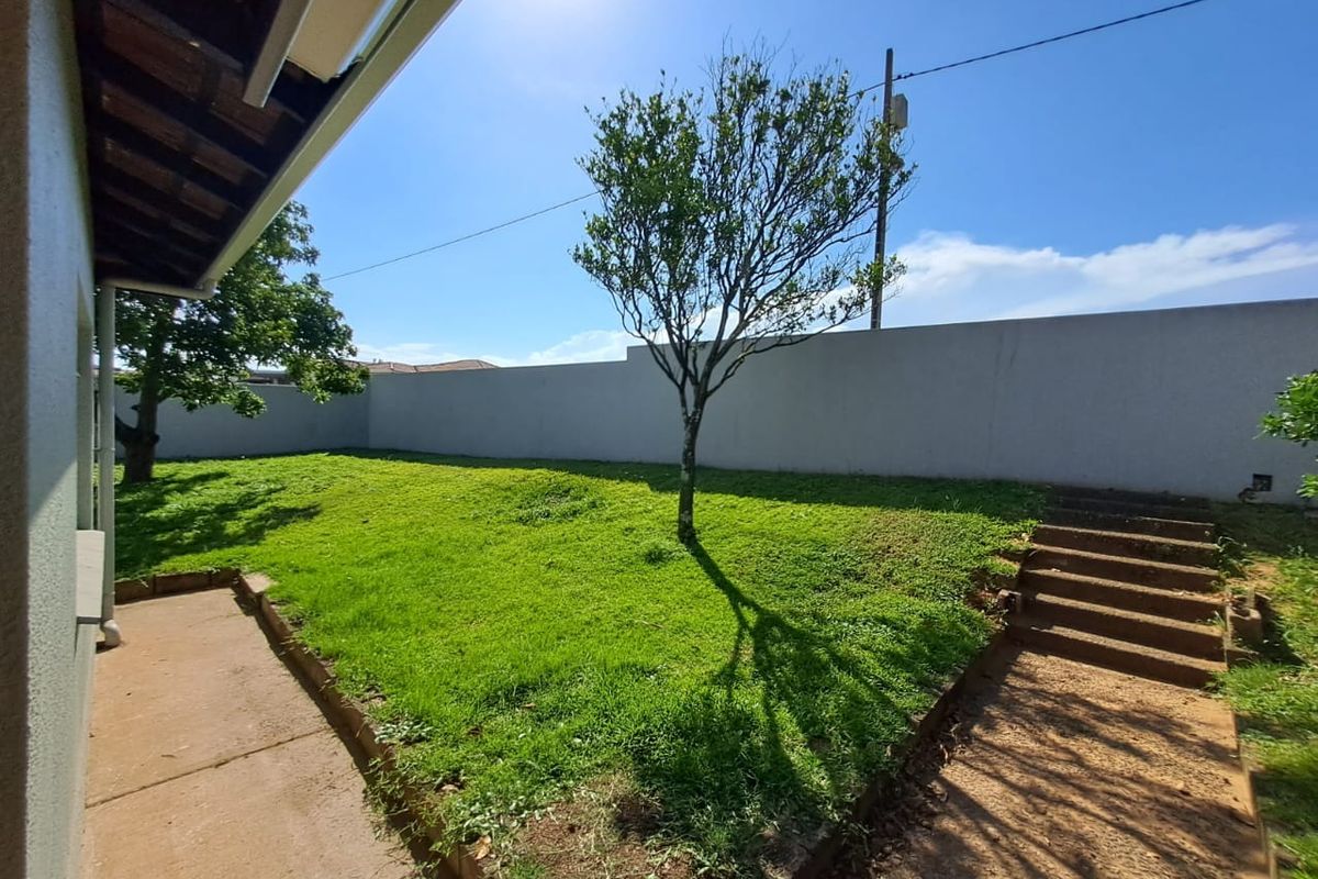A private rear garden featuring a lawn area, concrete boundary wall, and concrete steps leading to an elevated section of the yard.