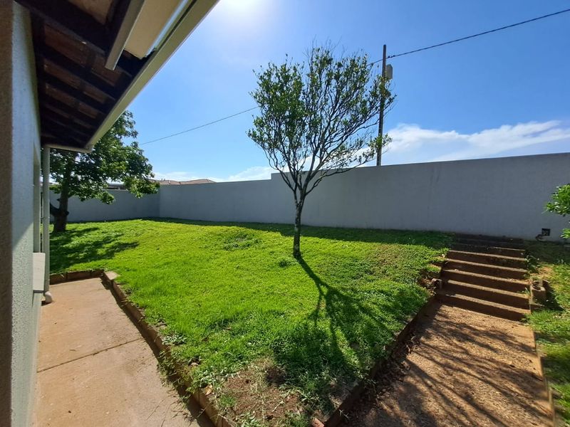 A private rear garden featuring a lawn area, concrete boundary wall, and concrete steps leading to an elevated section of the yard.