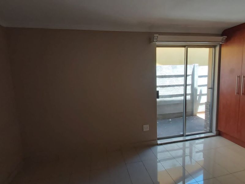 A bright, empty bedroom featuring tiled flooring, a built-in wooden wardrobe, and a sliding glass door providing access to an outdoor area.