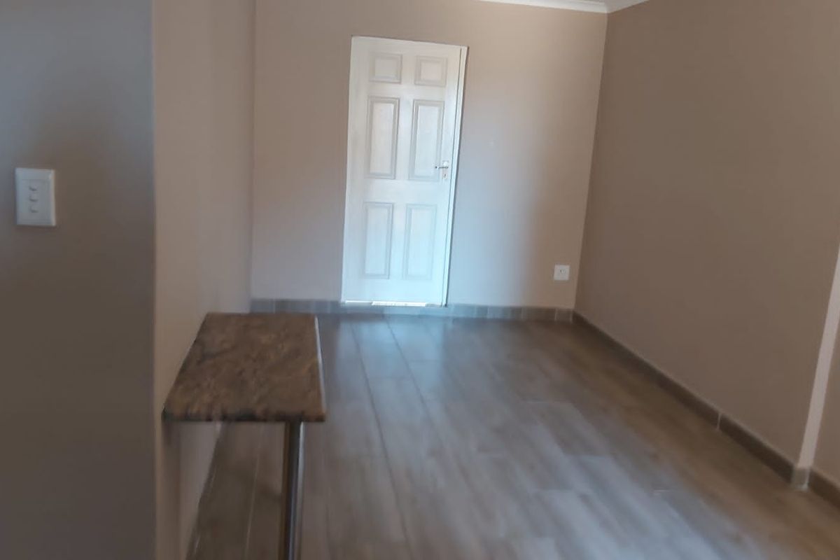 A clean, empty bedroom featuring neutral wall tones, wood-look tiled flooring, and a built-in wall-mounted shelf.